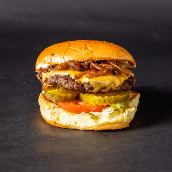 A Stack'd Burger with melted cheese, caramelized onions, pickles, tomato, and lettuce on a bun.