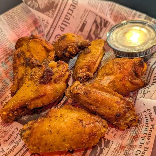 Crispy golden-brown chicken wings with seasoning and a side of dipping sauce, served on newspaper-print paper.