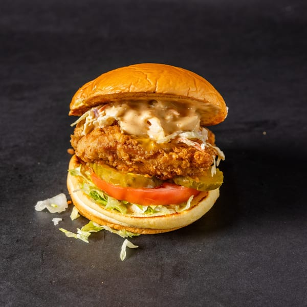 A Stack'd Burger fried chicken sandwich with coleslaw, pickles, tomato, and lettuce on a brioche bun.
