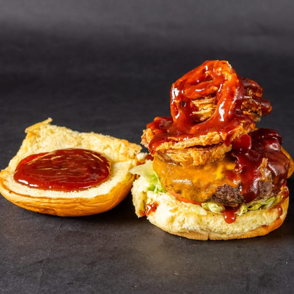 Stack'd Burger with melted cheese, onion rings, and barbecue sauce, with an open bun.
