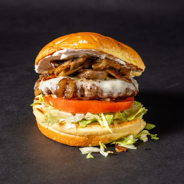 A Stack'd Burger with melted cheese, sautéed mushrooms, tomato, and lettuce on a dark background.